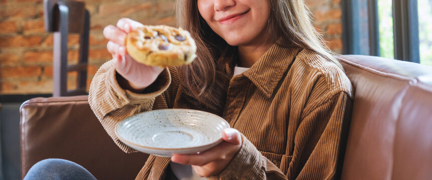 Closeup image of a young woman holding and eating at a piece of chocolate chip cookie