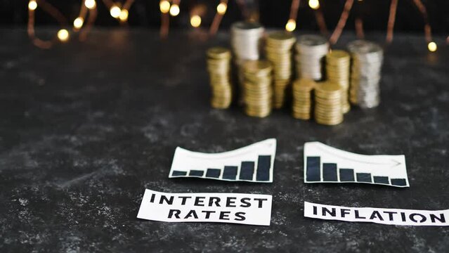 interest rates and inflation texts and graphs showing rates going up and consumer spending going down in front of stacks of coins