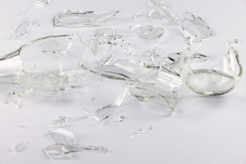 A glass bottle broken into many fragments on a gray background.