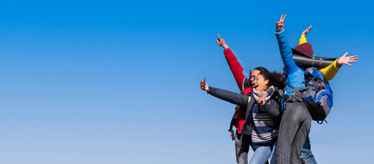 Multiracial group of hikers taking selfie on top of the mountains - Happy friends with hands up having fun together - Multiethnic people having trekking day out together
