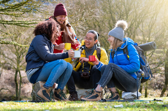 Multicultural group of hikers sitting on top of the mountain drinking coffe with backpacks - Happy hipster friends having trekking day out together - Travel and camping concept