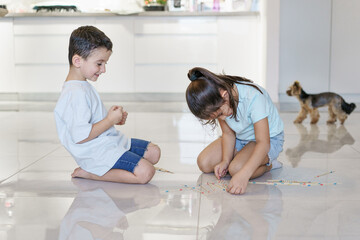 Happy children playing mikado in the fllor of living room at home, close up. Kids spending time...