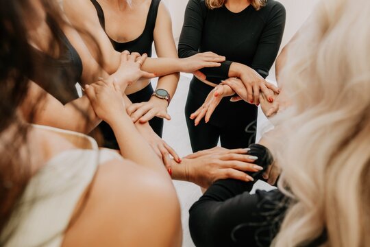 Partnership and unity concept: unrecognizable women in sportswear holding wrists of each other, forming circle. Group of happy young womans holding hands. Side view on human hands. Selective focus