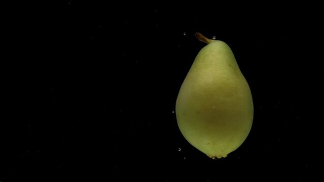 Slow motion one pear spinning falling into transparent water on black background. Fresh fruit splashing in aquarium. Organic fruit, healthy food, diet, fructose
