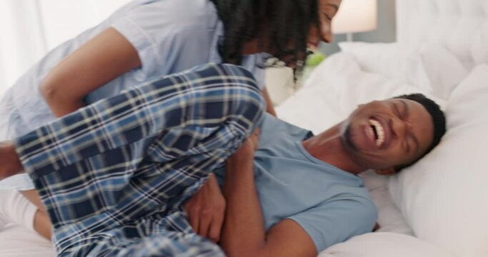 Funny, playful and happy black couple on bed tickling, teasing and having fun on bed for morning bonding, love and laughing. Healthy marriage of man and woman together in bedroom apartment in a hotel