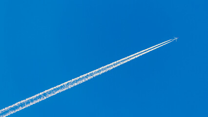 Airplane at cruising altitude with long white contrail in blue sky