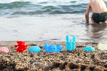 sands beach toys in a row against sea water and kid little boy is playing in background.shell...