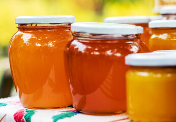 some honey jars in a row on table for sale outside city day festival national holiday.beekeeper natural bio eco organic product healthy.orange yellow color tasty delicious food.different size jars