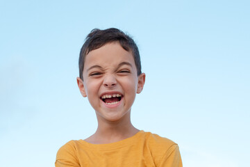 Cheerful positive child, blue sky on the background. Funny face of a boy 8 years old. Emotion, facial expression, holidays, funny kid face, life concept. Isolated. Brunette person, caucasian.