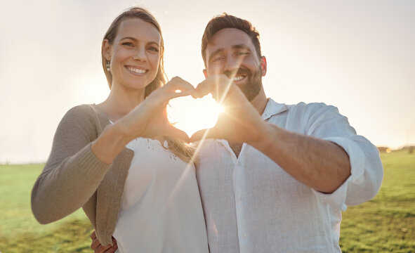 Couple, portrait and heart hand with sun for romantic date on beautiful field in Ireland. Love, happy and smile of dating people enjoying countryside together with natural sunshine flare.