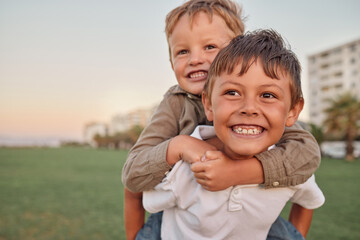 Happy, smile and portrait of brothers with piggyback ride playing in a park together on vacation....