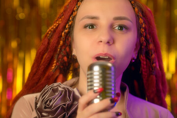 Young woman with ginger dreadlocks singing into microphone. Portrait of female singer with microphone in studio.