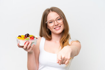 Young pretty woman holding a bowl of fruit isolated on white background points finger at you with a confident expression