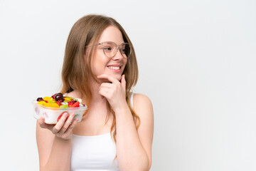 Young pretty woman holding a bowl of fruit isolated on white background thinking an idea and looking side