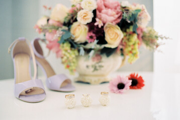 Wedding rings lie on sweets on the table near the bouquet of flowers and the bride shoes