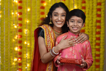 Young woman and son celebrating diwali,holding plate of diyas, gift boxes 