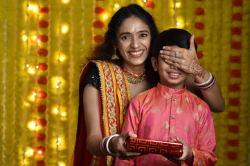 Young woman and son celebrating diwali,holding plate of diyas, gift boxes 