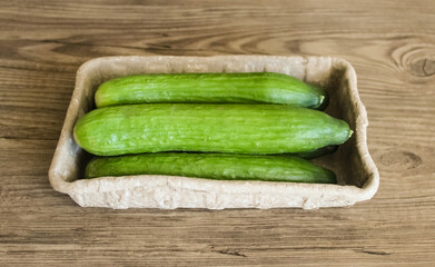 Cucumbers in recycled packaging on wooden background