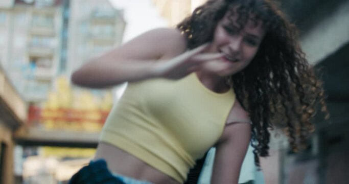 Two young girls come together to practice choreographed dance together on a street in the city. The curly-haired teens dressed in loose clothing move to the rhythm of music from a loudspeaker.