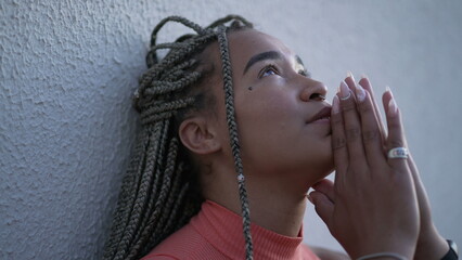 One spiritual young black woman praying to God pleading help and support. A faithful Brazilian adult girl in prayer looking up at sky with HOPE and FAITH - obrazy, fototapety, plakaty