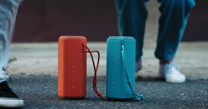 Close-up of two color speakers standing on the asphalt of the street. Around the music speakers can be seen the feet and sneakers of women dancing.