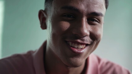 One happy hispanic young man closeup face. Portrait of a South American Brazilian male person looking at camera smiling indoors
