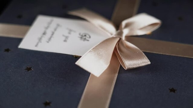 A gift in a box tied with a golden ribbon with a bow and a message rotates on a black background 4k