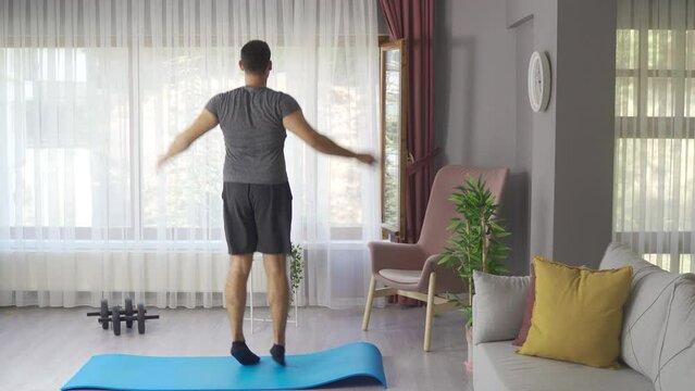 Sport, fitness and healthy lifestyle concept.
Young man doing jumping jack exercise at home.
