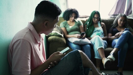 Fototapeta premium One hispanic man looking at cellphone device in foreground. Three female black friends in background using phones