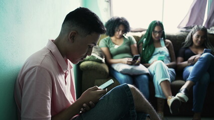 One hispanic man looking at cellphone device in foreground. Three female black friends in background using phones