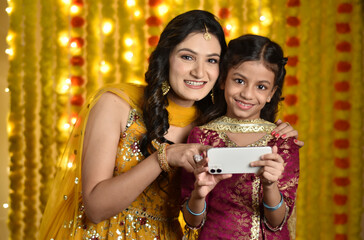 Happy young woman and daughter celebrating diwali and taking selfie