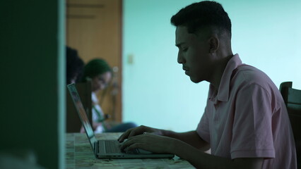 One candid hispanic man in front of laptop typing on keyboard and browsing internet