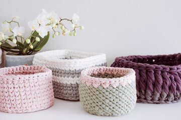 Fototapeta na wymiar White orchid, green, pink and purple cute decorative hand crocheted baskets. Cozy home atmosphere with decorative purple dry plants and white background
