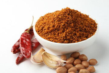 Powdered Garlic, coconut Chutney in a white bowl with garlic cloves, red chilies and groundnuts all places on a white background 