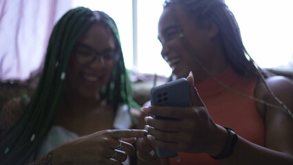 Girlfriends pointing at cellphone screen laughing and smiling. Two young female friends holding phone