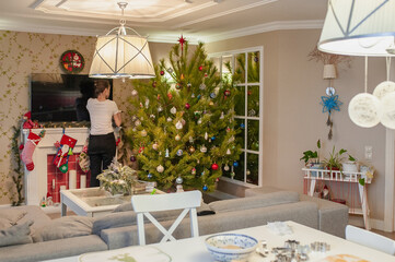 A woman is cleaning in a Christmas interior with a Christmas tree and a fireplace
