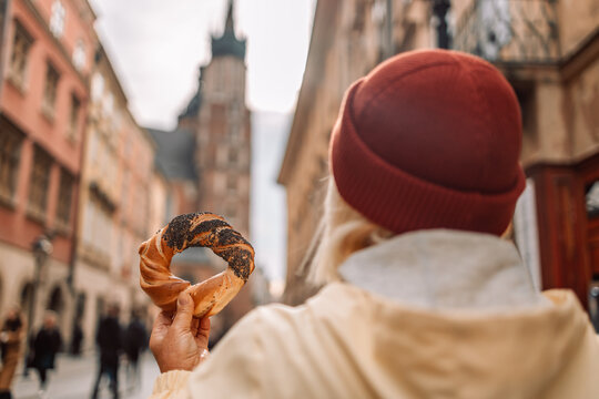 Tourist woman hand holding bagel obwarzanek, traditional polish snack in old city center view in Krakow, Europe. Back view