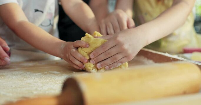 Selective focus close up shot on wooden table with homemade dough. Older sister daughter helping preschooler girl kneading dough for baking cooking domestic cookies pasta pizza biscuits at home.