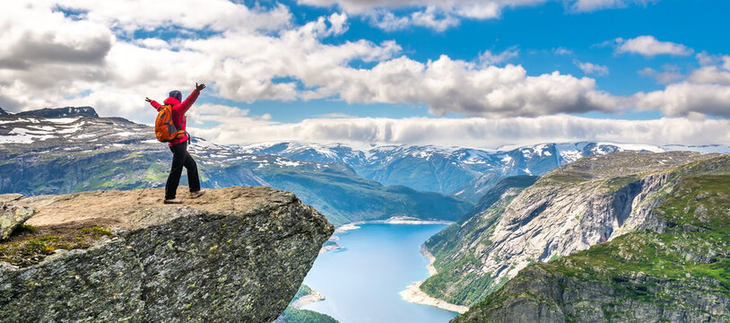 Hiker woman stands at rock and looks at aerial view in the mountains. Amazing nature view on the way to Trolltunga. Location: Scandinavian Mountains, Norway, Odda. The feeling of complete freedom