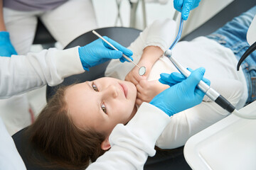 Pedodontist treating little patient teeth assisted by nurse