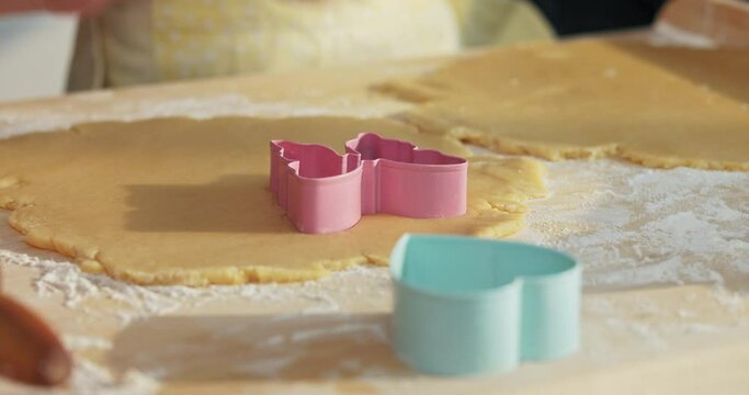 Close up shot colorful cookies cutters on wooden surface. Woman's hands pressing homemade domestic dough making cookies in different shapes teaching preschooler granddaughter baking cooking dessert.