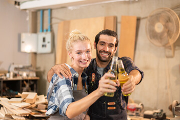 Happy couple carpenter drinking after work finish together in wood workshop