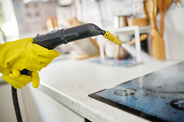 The steam generator washes the dirty electric stove. Hot steam White kitchen. Cleaning