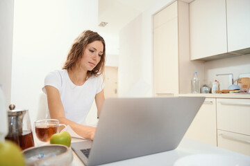 Fototapeta premium Woman is typing on laptop keyboard at kitchen table