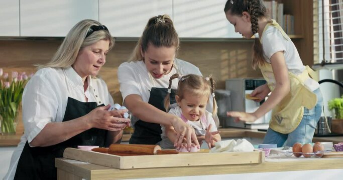 Happy family young mother elderly grandmother and shooler kids learning how to make cook bake homemade domestic cookies biscuits . Middle aged granny putting cookies in different shape on tray.