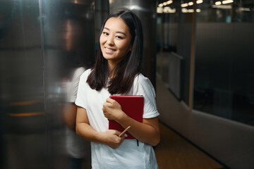 Happy cheerful Asian woman standing near the glass door and posing