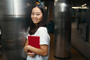Smiling woman with notebook in hand standing near the glass door in office