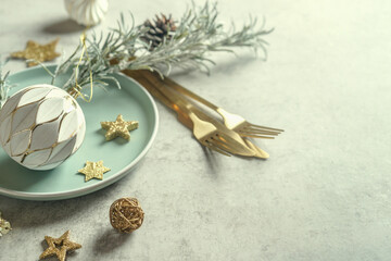 Fototapeta na wymiar Christmas table setting for vestive dinner with plate, golden cutlery and decoration of vintage bauble, stars and pine branches