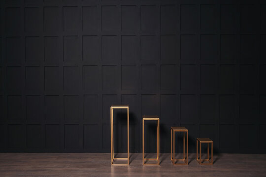 golden iron racks on a black background. square columns against a black wall in a photo studio. gothic style wedding photo zone
