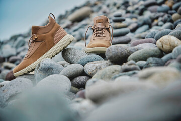 A pair of brown leather waterproof trekking boots on a sea coast. Hiking concept.